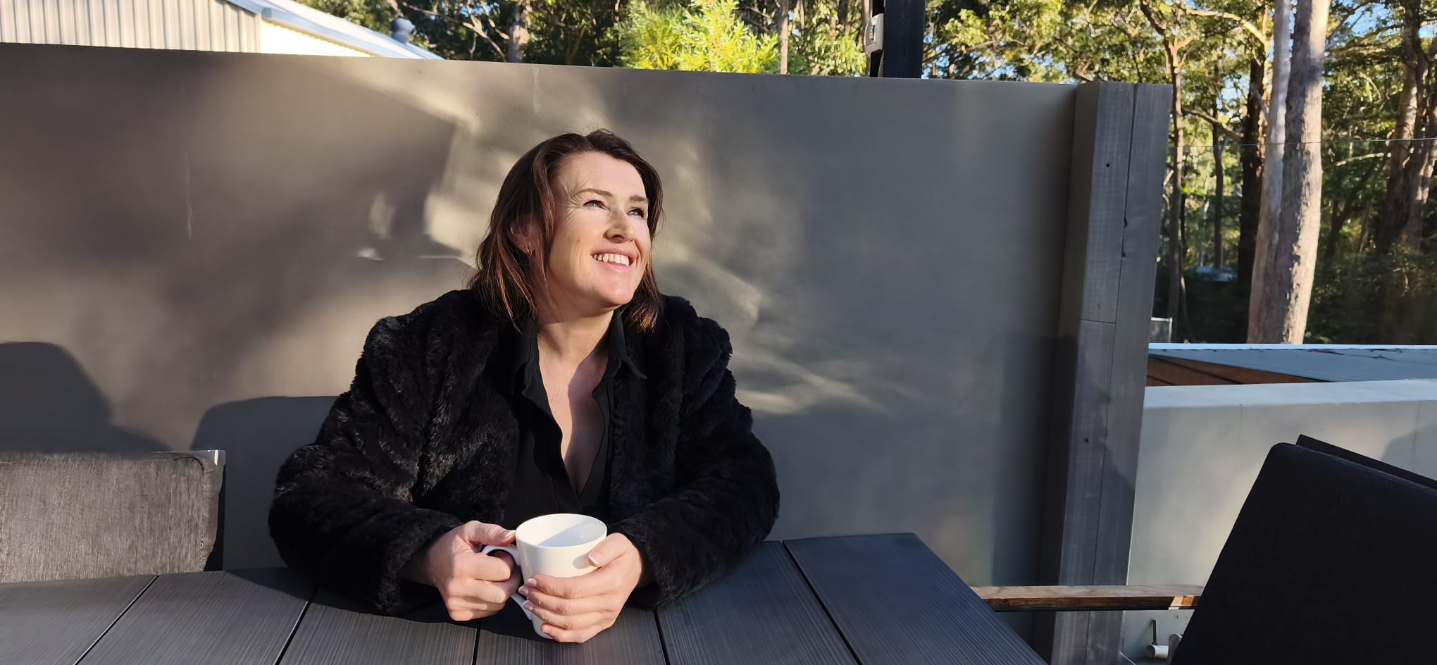 Shelle Blyth, smiling with a cup of tea in the morning sun